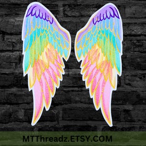 May include: A pair of embroidered angel wing patches featuring a vibrant rainbow gradient of purple, blue, teal, yellow, and pink threads with gold-colored outlines. The wings are symmetrical and detailed with individual feather stitching patterns.
