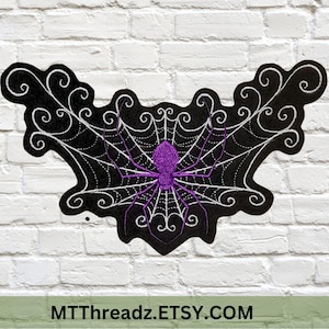 May include: A black embroidered patch featuring a purple spider in a web design. The spider web is white, and the patch has a decorative border. The text "MTThreadz.ETSY.COM" is at the bottom.