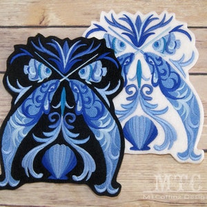 May include: Two embroidered patches featuring an owl design. One patch is black with blue and light blue details, the other is white with blue and light blue details. The owl design includes floral and seashell motifs.