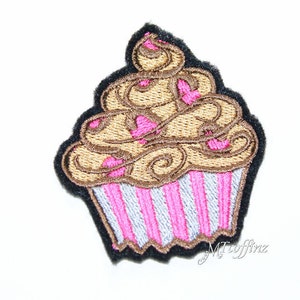 May include: An embroidered cupcake patch in brown and pink, featuring a swirl design and pink hearts. The cupcake is set against a black background.