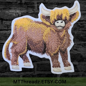 Peut inclure: Patch brodé représentant une vache Highland brune et jaune sur fond blanc. La vache a une longue robe hirsute et un visage blanc. Le patch mesure environ 10 cm de large et 7,5 cm de haut.