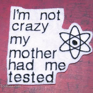 May include: White fabric patch with black embroidered text that reads "I'm not crazy my mother had me tested" and a black embroidered atom symbol.