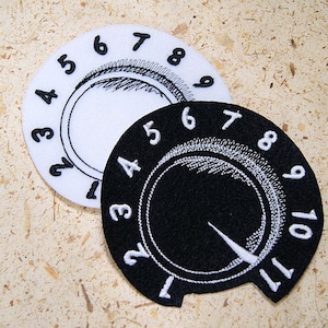 May include: Two round, white and black fabric patches with numbers 1 through 11 around the edge. The white patch has a black circle in the center with a scribbled design. The black patch has a white circle in the center with a white arrow pointing to the right.