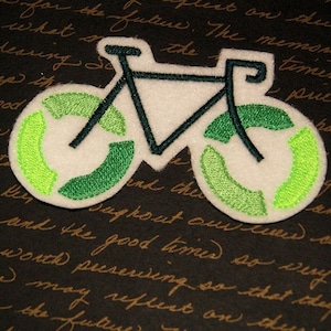 May include: A white bicycle patch with green and lime green accents. The wheels are designed with a recycling symbol. The bicycle frame and details are dark green. The patch is on a dark background with handwritten text.