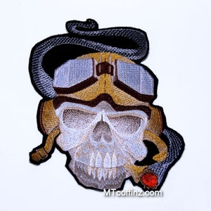 May include: Embroidered patch of a skull wearing aviator goggles and a scarf, with a cigarette in its mouth. The skull is white with brown and gold accents. The scarf is black and the cigarette is red.