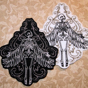 May include: Two embroidered patches featuring a skeleton with wings. The skeleton is in a black and white design. The patches are on a brown background.