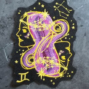 May include: Embroidered Gemini zodiac sign patch with two faces and a constellation of stars in gold and purple on a black background. The patch has the Gemini symbol "II" in gold.