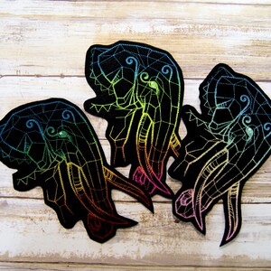 May include: Three embroidered iron-on patches featuring a geometric design of an elephant with rainbow colored thread. The patches are on a light wood background.