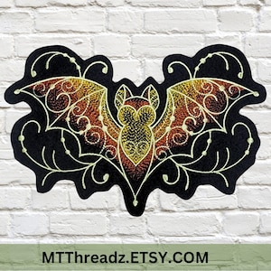 May include: Black bat-shaped embroidered patch with intricate gold, orange, and red wing details. The bat has a detailed body and is surrounded by a decorative, swirling design. The text "MTThreadz.ETSY.COM" is at the bottom.