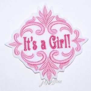 May include: Pink embroidered patch with a decorative floral design and the text "It's a Girl!"