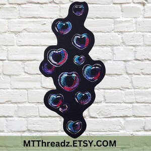 May include: Black embroidered patch featuring a cluster of colorful heart-shaped bubbles. The bubbles have a rainbow effect with shades of blue, pink, and purple. The patch is against a white brick wall. Text at the bottom reads MTThreadz.ETSY.COM.