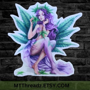 May include: A purple fairy with green wings sits on a bed of green leaves. She is holding a green leaf in her hand and has a crown of green leaves on her head. The background is a brick wall.