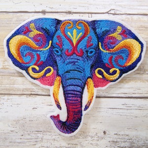 May include: Embroidered patch of an elephant with intricate floral designs in shades of blue, yellow, red, and purple. The elephant's trunk is curled up and its eyes are closed.