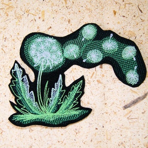 May include: Green embroidered iron-on patch of a dandelion with a black background. The dandelion has a white center and green leaves.