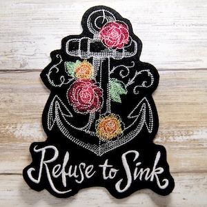 May include: Black felt patch with a white embroidered anchor surrounded by colorful flowers and the text "Refuse to Sink".
