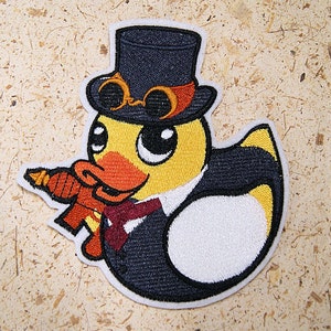 May include: A yellow rubber duck wearing a black top hat with goggles and a red bow tie. The duck is holding a red and orange carrot in its beak.