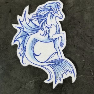 Peut inclure: Patch brodé bleu d'un hippocampe avec une crinière flottante et une queue de poisson.