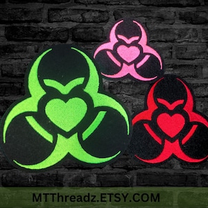 May include: Three embroidered patches featuring a biohazard symbol with a heart in the center. The patches are in neon green, pink, and red, each on a black background. The text "MTThreadz.ETSY.COM" is at the bottom.