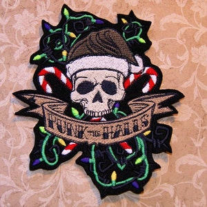 May include: A black and white embroidered patch with a skull wearing a Santa hat and surrounded by candy canes and Christmas lights. The banner reads "Funny the Halls".