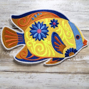 Peut inclure: Un poisson brodé jaune avec des détails bleus et orange. Le poisson a un motif floral avec des fleurs bleues et des centres roses.