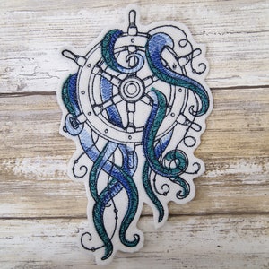 May include: Embroidered patch featuring a white ship's wheel with blue and green tentacles wrapping around it. The patch is on a white background.
