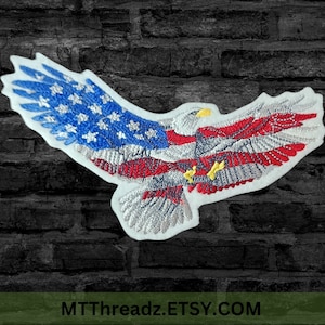 May include: Embroidered patch of a bald eagle with wings spread, flying with the American flag design. The eagle is silver, the flag is red, white, and blue.