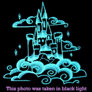 May include: A glowing blue castle with white towers and windows, surrounded by clouds, against a black background. The image was taken under a black light.