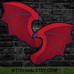 Puede incluir: Dos alas bordadas de color rojo con contornos negros y un centro azul. Las alas est&aacute;n curvadas y se superponen. El fondo es una pared de ladrillo oscuro. El texto "MTTThreadz.ETSY.COM" est&aacute; en la parte inferior de la imagen.