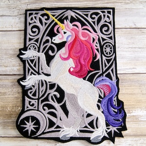 May include: Embroidered iron-on patch featuring a white unicorn with a pink and purple mane and tail, standing within a silver and black ornate frame.