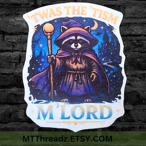 May include: A die-cut sticker featuring a raccoon dressed as a wizard in a purple robe and hat, holding a golden staff. The background shows a dark blue night sky with a castle and stars. The text reads 'TWAS THE 'TISM M'LORD' in yellow and blue.
