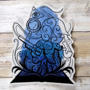 May include: Embroidered patch featuring a blue and black design of a diver with a helmet and scuba gear, surrounded by swirling patterns and a book.