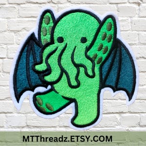 May include: Green embroidered patch of a cartoon Cthulhu with bat wings. The patch has a white outline and is on a white brick background.