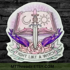May include: A sticker featuring a fantasy design with a book, sword, moon, and sun. Purple hands hold the book, with roses below. The banner reads "FIGHT LIKE A WITCH". The design has a watercolor effect.