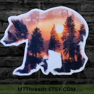 May include: A silhouette of a bear with a sunset and forest scene inside. The bear is walking towards the right side of the image. The sunset is orange and red with a bright yellow sun. The forest is dark green with tall trees.