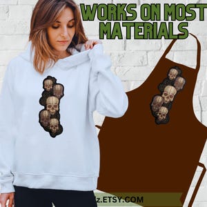 K&ouml;nnte beinhalten: Ein wei&szlig;er Hoodie mit einem Design aus f&uuml;nf Sch&auml;deln in einer vertikalen Reihe. Der Text "WORKS ON MOST MATERIALS" ist im Hintergrund sichtbar.