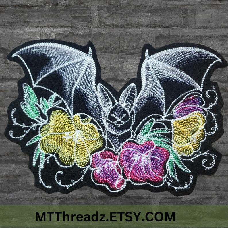 May include: Embroidered patch showing a bat with white wings and a black body, framed by flowers in yellow, pink, and purple. The patch has the text "MTThreadz.ETSY.COM" at the bottom. The design is on a black background.