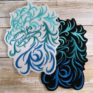 May include: Two embroidered iron-on patches featuring a stylized dragon design. The patches are made of felt and have a white background with blue and green embroidery. One patch has a black background with blue and green embroidery.