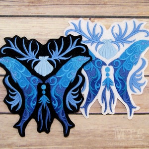 May include: Two embroidered patches depicting a stylized butterfly with blue and teal gradient wings, a seashell, and antlers. The patches are on a wooden background.