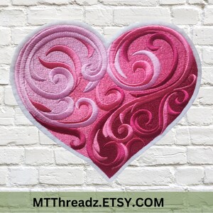 May include: A pink and red embroidered heart with a white outline and intricate swirling designs. The heart is on a white brick background.