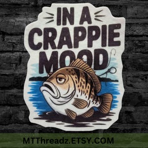 May include: A white sticker with a cartoon crappie fish and the text "In a Crappie Mood". The fish is brown and white with a blue background.
