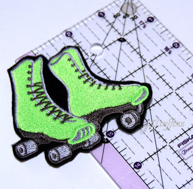 May include: A pair of green roller skates with black wheels and silver accents. The skates are embroidered and have a vintage style.