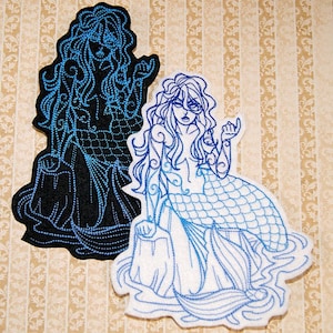 May include: Two embroidered patches of a mermaid with long hair and a tail. The mermaid on the left is black with blue stitching. The mermaid on the right is white with blue stitching.