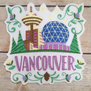 May include: Embroidered patch featuring Vancouver landmarks, including a tower and a geodesic dome. The patch is white with green, purple, yellow, and brown embroidery. The word "VANCOUVER" is stitched in purple.