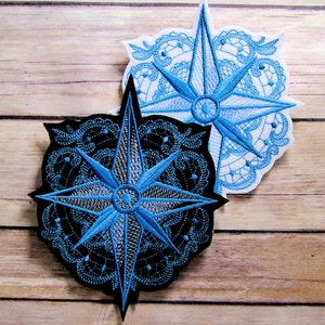 May include: Two embroidered patches featuring a blue compass rose design. The compass rose is surrounded by a black and white lace design on one patch and a white lace design on the other.