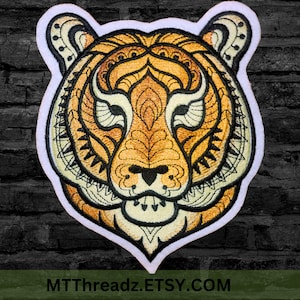 May include: Iron-on patch featuring a detailed mandala-style tiger head design in shades of orange, yellow, and black. The patch has a white border and is perfect for adding a unique touch to clothing, bags, or other accessories.