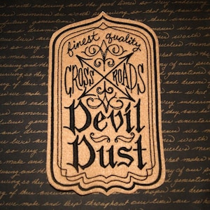 May include: A brown, rectangular patch with black embroidered text that reads "finest quality Crossroads Devil Dust".