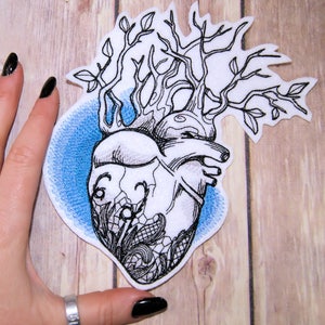 May include: Embroidered iron-on patch featuring a black and white anatomical heart with a tree growing out of it. The heart is surrounded by a blue circle.
