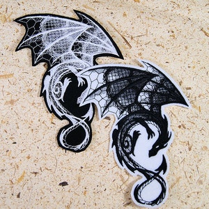May include: Two black and white embroidered iron-on patches of dragons. One dragon is white with black details and the other is black with white details.