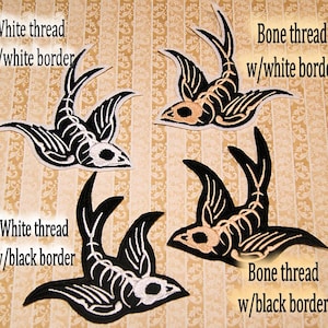 May include: Four embroidered iron-on patches of a skeleton bird in flight. Two patches are white thread with a white border, and two patches are white thread with a black border.