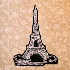 May include: White embroidered iron-on patch of the Eiffel Tower on a black background. The patch is approximately 4 inches tall.